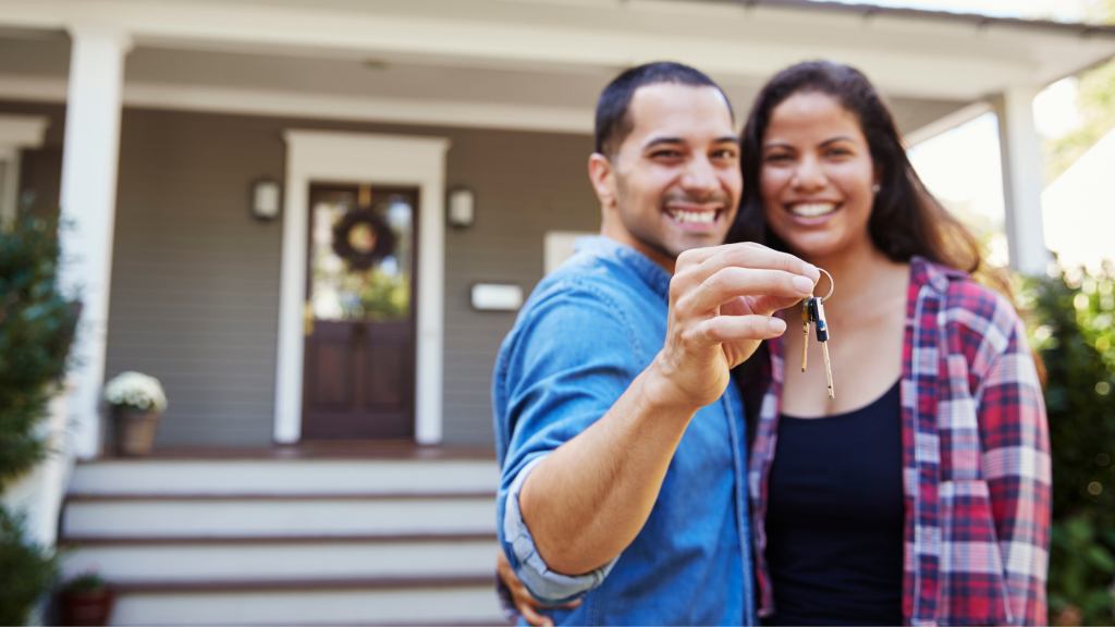 August 2026 | Flader Plumbing Smiling couple holding up keys in front of their home, celebrating a new house.